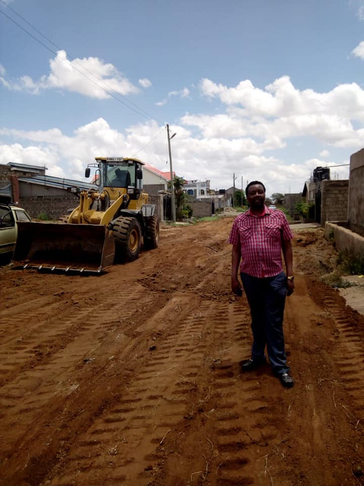 Pastor Godfrey Migwi stands next to a heavy construction vehicle that was fixing a public road he paid for with his own money